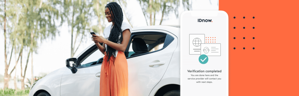 woman looking at her phone standing next to a white car with a sign that says verification completed