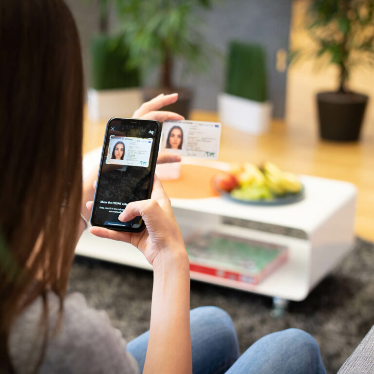 woman sitting in a living room taking a picture of her ID with her smartphone.