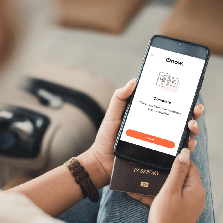 person holding a phone over a passport with IDnow complete verfication on screen