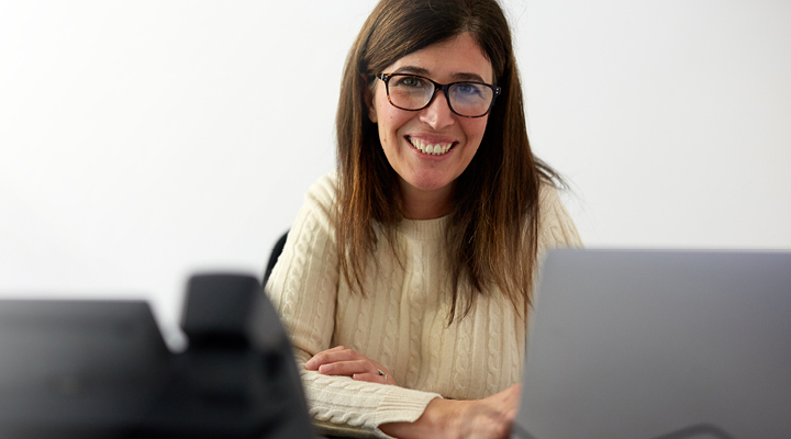 woman in tan sweater and glasses smiling looking at the camera