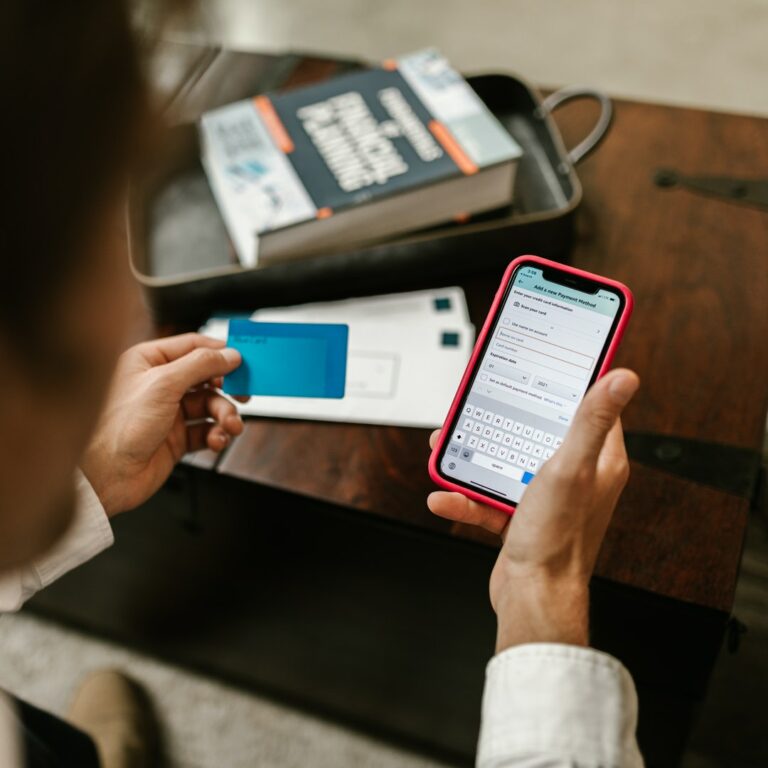 man looking on smartphone with a blue card in his left hand