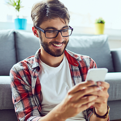 man sitting in a living room looking at his phone smiling