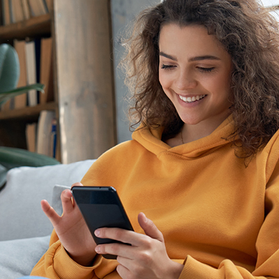 woman wearing yellow hoodie looking at her phone smiling