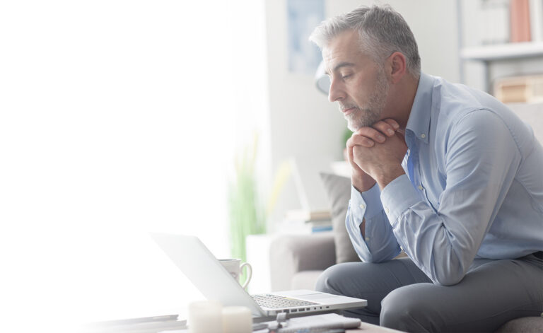 man in blue button-down shirt sitting on sofa in front of laptop with his head resting on his hands