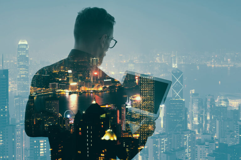 man standing in a building facing on a city view with a laptop in his hand