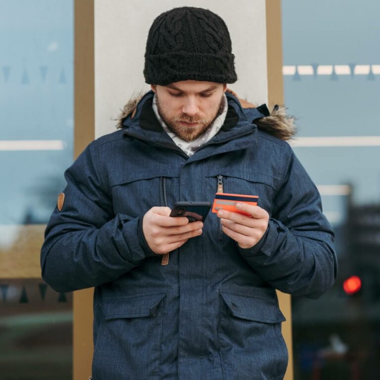 man wearing a coat holding a phone in his right hand and an orange card in his left hand