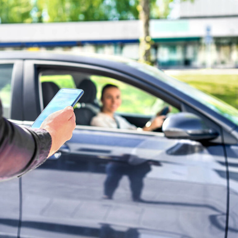 a hand with a phone in front of a car with a woman driving