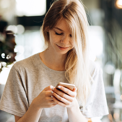 woman wearing gray tshirt looking at her phone smiling