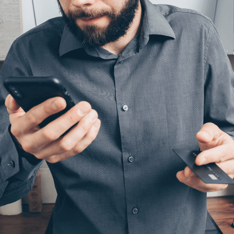 man in grey button-down shirt with phone in one hand and credit card in the other